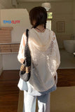 Person wearing a sheer white top and holding a black and brown bag in a room with shelves and a bathtub.