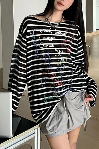 Person wearing a black and white striped sweater with colorful text and gray shorts indoors.