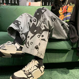 Person wearing a graphic t-shirt and pants with sneakers, sitting on a green couch.