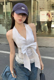 Woman wearing a white sleeveless top with a bow and blue jeans, standing on a street.