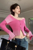 Woman wearing a pink off-shoulder sweater and blue jeans, holding a black handbag.
