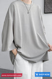 Person wearing a gray oversized shirt and white pants against a plain background with 'tomscloth.com' branding.