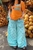 Person wearing an orange shirt with text and light blue polka dot pants standing among stacked coconuts.