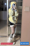 Person wearing a yellow hoodie with a bear design, taking a mirror selfie in a kitchen.