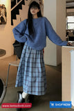 Woman in a blue sweater and plaid skirt standing indoors with a 'Shop Now' button visible.