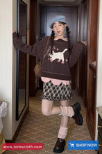 Person wearing a sweater with a cat design in a hallway, with 'www.tomscloth.com' branding.