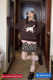 Person wearing a sweater with a cat design in a hallway, with 'www.tomscloth.com' branding.