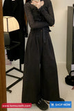 Person wearing a dark gray outfit with wide-leg pants in a store setting.