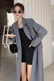 Woman wearing a long gray coat and black outfit indoors.