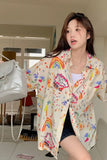 Woman wearing a colorful jacket with cartoon designs in a room.