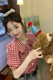 Woman in a red and white checkered shirt holding a teddy bear indoors.