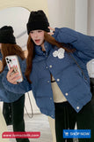 Woman taking a mirror selfie wearing a blue jacket with floral details and black beanie.