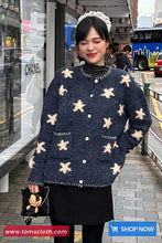 Woman wearing a navy blue sweater with white floral patterns at a bus stop, with 'Toms Cloth' branding visible.