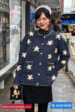 Woman wearing a navy blue sweater with white floral patterns at a bus stop, with 'Toms Cloth' branding visible.