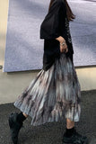 Person wearing a black top and pleated skirt with abstract pattern on a street.
