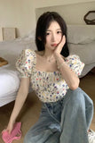 Woman sitting on the floor wearing a floral top and jeans in a bedroom setting.