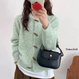 Person wearing a light green knitted cardigan with brown buttons, holding a black handbag.