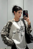 Person wearing a camouflage jacket and white graphic t-shirt, taking a mirror selfie.