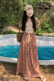 Woman in a plaid skirt and cap standing by a pool with greenery in the background