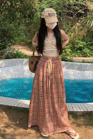Woman in a plaid skirt and cap standing by a pool with greenery in the background