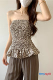 Woman wearing a leopard print strapless top and brown pants against a plain background