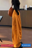 Person wearing mustard yellow pants and a brown bag in an indoor setting