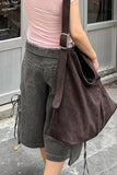 Person wearing a pink shirt and gray shorts with a brown bag outdoors.