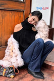Woman sitting on a wooden floor with a fur coat and handbag, wearing a black sweater and blue jeans. TOMS CLOTH brand visible.