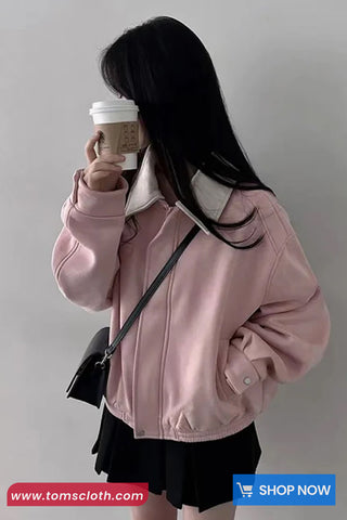 Person wearing a pink jacket holding a coffee cup against a plain background