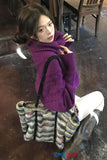 Woman in a purple sweater sitting on a chair with a colorful bag next to her.