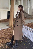 Person wearing a long brown coat and black boots standing outdoors.