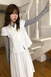 Woman in a white dress standing in a room with wooden floors and white walls.