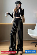 Person wearing a stylish outfit with wide-leg pants, holding a coffee cup in an indoor setting.