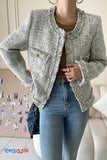 Person wearing a textured gray jacket with button details, standing in a room with a couch and decorative items.
