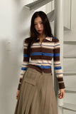 Woman wearing a striped sweater and beige skirt standing in a minimalistic room.