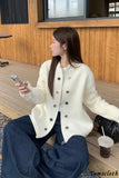 Woman in a white coat sitting on a wooden bench with a drink and phone.