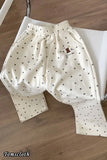 White polka dot pants with a small logo on a wooden floor, brand 'Tomscloth' visible.