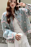 Woman wearing a floral embroidered jacket holding a drink.