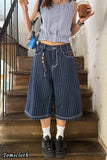 Person wearing a blue checkered top and pinstripe pants standing on wooden stairs.