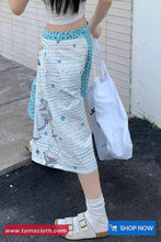 Person wearing a patterned skirt and holding a white bag on a sidewalk.