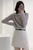 Person wearing a gray sweater and skirt in a minimalistic setting