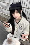 Person wearing a black cap and checkered jacket with a stuffed animal, sitting on a concrete surface.
