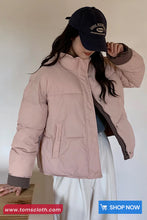 Person wearing a pink puffer jacket and black cap with 'John Kerry' text, standing against a plain background.