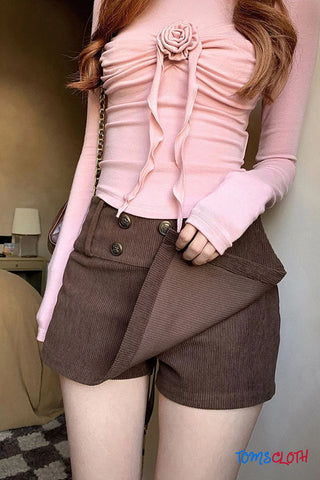 Person wearing a pink top with a rose detail and brown shorts, holding a handbag.