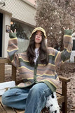 Person wearing a striped sweater and sitting outdoors on a wooden bench.