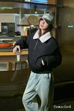 Person wearing a black jacket with white collar and light blue pants in a casual setting.