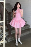 Woman in a pink checkered dress standing on a staircase holding a drink.