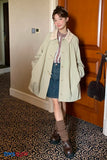 Woman in a coat standing in a room with a wooden door and patterned carpet.