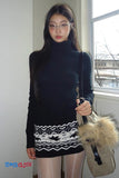 Woman wearing a black turtleneck dress with a patterned hem, holding a beige bag.