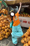 Person in orange shirt and blue pants standing among coconuts with a 'Coconut Day' sign in the background.